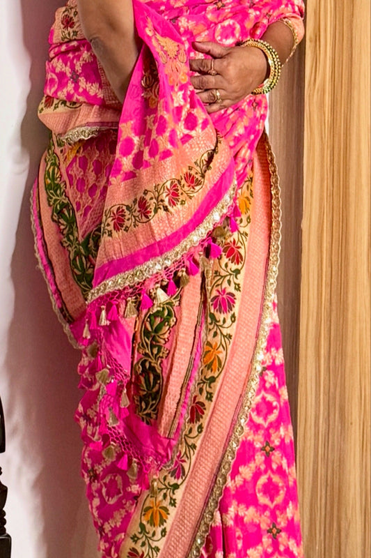 Bright pink saree with intricate gold and green patterns draped over a person.