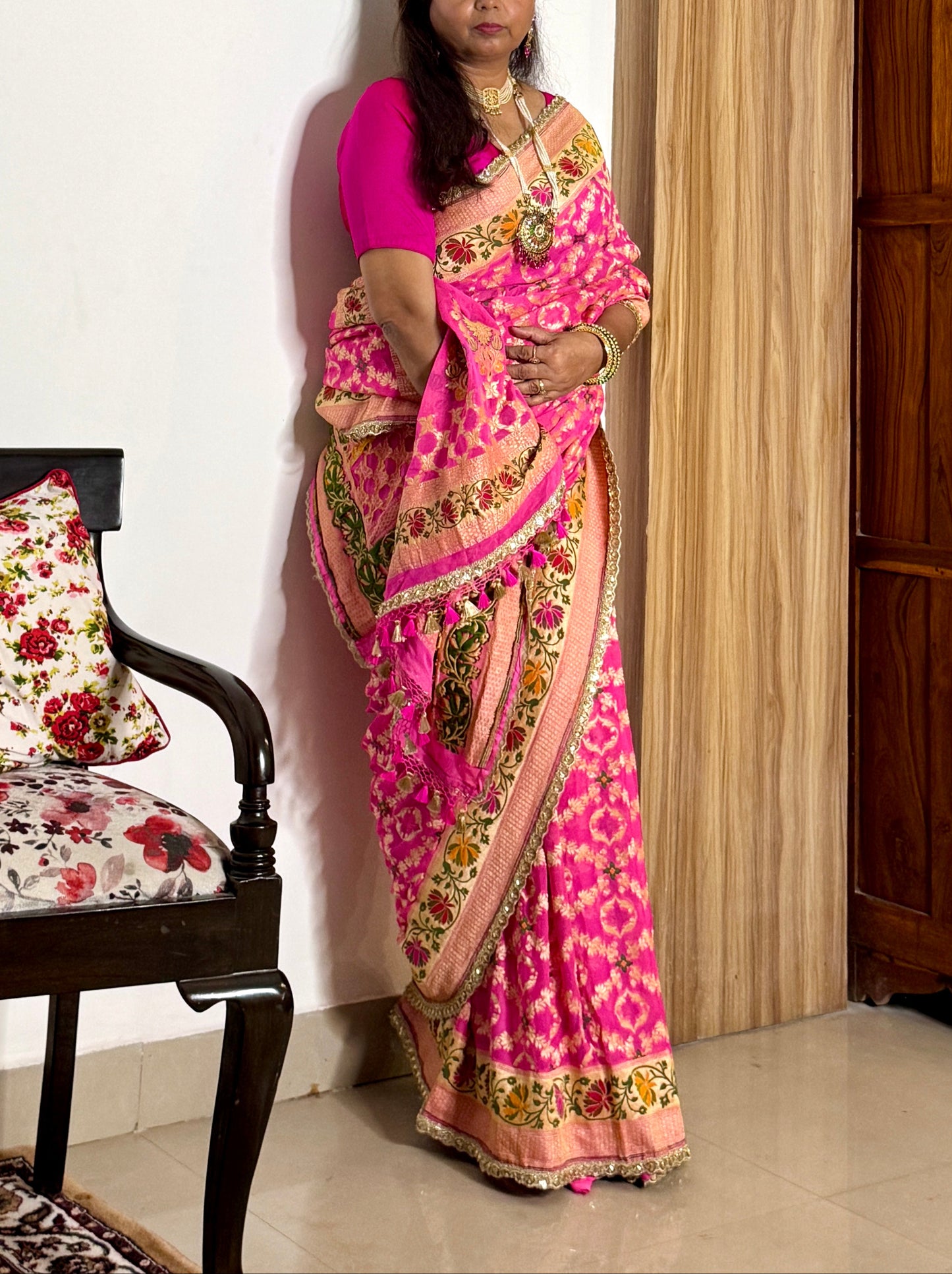 Woman wearing a pink saree with a floral pattern in a room.